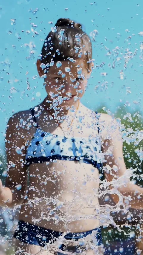 Smiling, happy eight year old girl in swimsuit having fun in splashes in street Stock Footage 316262067