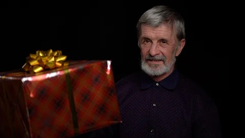 Smiling happy elderly man with a present gift box on black background. Stock Footage 122050423