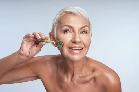Smiling happy lady using jade roller on her face Foto stock