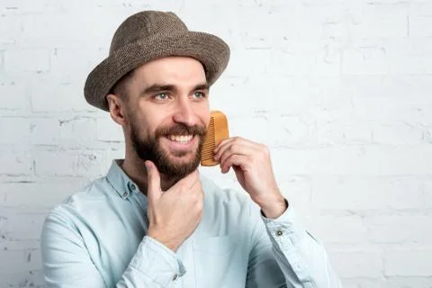 Smiling happy man in hat comb his beard closeup. Stock Photos