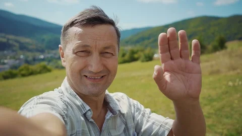 Smiling happy man look at camera waving his hand background mountains summer Stock Footage 116997807