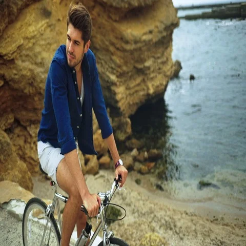 Smiling happy model posing with a bicycle on the stony beach Stock Footage 69296892
