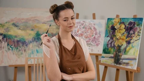 Smiling happy painter with a paintbrush in hands posing on camera in art studio Stock Footage 74206197