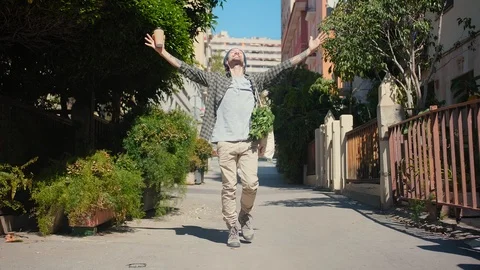 Smiling Hispanic guy listening positive music with earphones and walks dancing Stock Footage 108435715