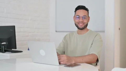 Smiling Hispanic Man Looking at Camera at Workspace Stockbeeldmateriaal 307904571