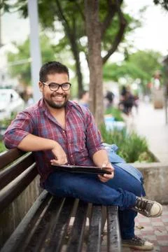 Smiling Hispanic man sitting on bench reading brochure Fotos de archivo