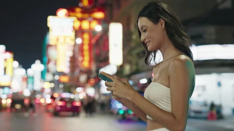 Smiling Hispanic woman using smartphone in vibrant city night scene Stock Footage 281731581