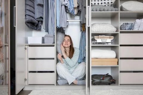 Smiling housewife in pajamas sleeping on pillow at wardrobe. Woman hiding in Stock Photos