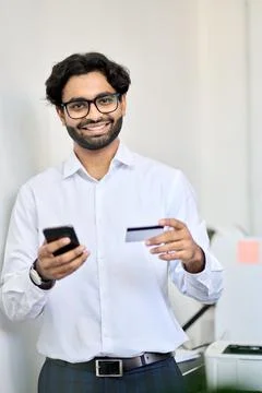 Smiling indian business man using phone holding credit card making e payment. Stock Photos
