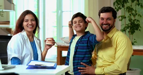 Smiling Indian dentist teaching young boy about strong teeth with a denture Stock Footage 342433790