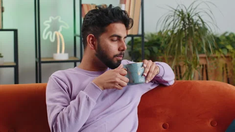 Smiling indian man drinking a cup of warm coffee or herbal tea at the morning at Stock Footage 243990465