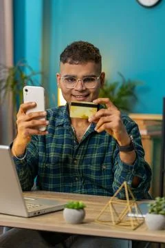 Smiling Indian man using bank credit card and smartphone for online shopping Stock Photos