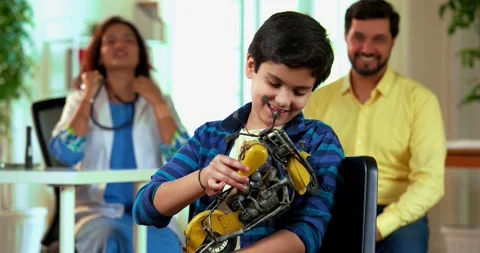 Smiling Indian young boy holds motorcycle toy while sitting in clinic as doctor Stock Footage 342433556