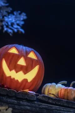 A smiling Jack O Lantern sitting on an old wooden porch with small pumpkins Foto stock
