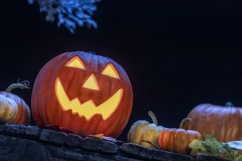 A smiling Jack O Lantern sitting on an old wooden porch with small pumpkins Foto stock