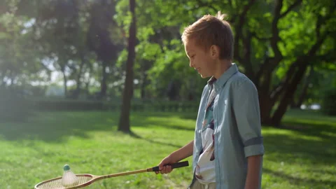 Smiling joyful boy put shuttlecock on racket. Kid play badminton on sunny day. Stock Footage 170514259