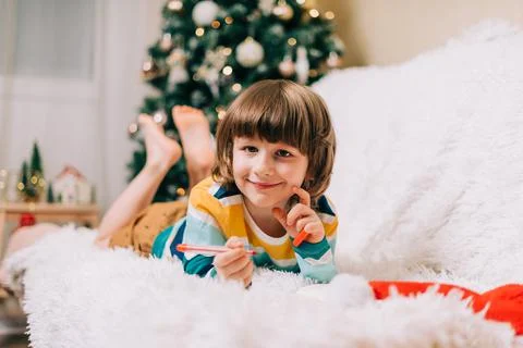 Smiling Kid boy lying on couch and writing the letter to dear Santa at home near Stock Photos
