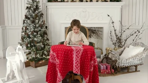 Smiling kid boy sitting at table and playing with tablet during Christmas time Vidéo 70897859