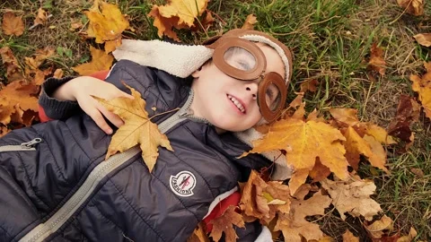 Smiling kid having fun. Boy lying on his back on autumn foliage Stock Footage 230120904