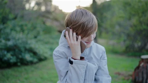 Smiling Kid on the Phone Talking in Green Park During Golden Hour Sunset. Vídeos de archivo 338140734