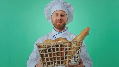 Smiling large baker man in a green studio holding a big basket full of fresh Stock Footage 125488274