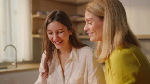 Smiling lesbian couple drinking wine sitting in kitchen relaxing at home. LGBT Video stock 260813718