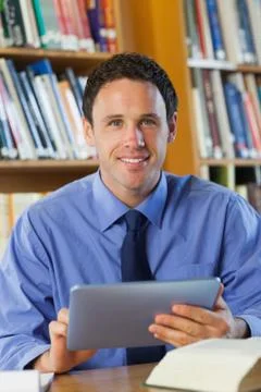 Smiling librarian sitting at desk using tablet Stock Photos