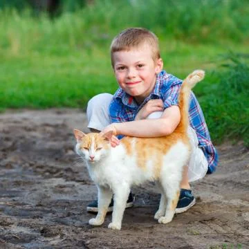 Smiling little boy affectionately embraces a red cat. outdoor Stock Photos