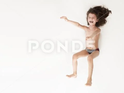 Smiling little boy in swimming trunks jumping with arms raised against a white Stock Photos