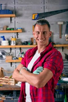 Smiling locksmith is standing in the workshop against the background of a wall Stock Photos