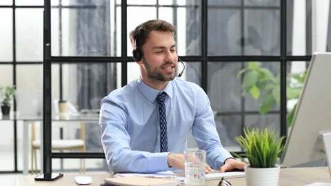 Smiling male call-center operator with headphones sitting at modern office Stock Footage 196863490