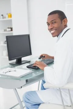 Smiling male doctor using computer at medical office Stock Photos