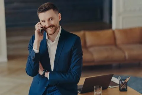 Smiling male entrepreneur talking on mobile phone while leaning on office desk Stock Photos