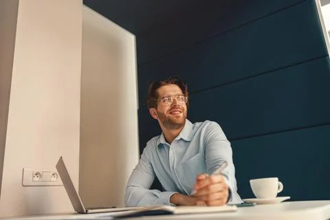 Smiling male freelancer making notes during working on laptop in coworking and Stock Photos