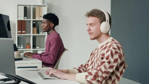 Smiling Male IT Developer in Headphones Writing Code on Computer at Office Desk Stock Footage 330126179