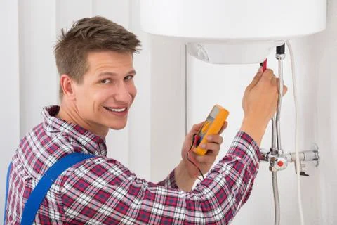 Smiling Male Plumber Examining Electric Boiler With Multimeter Probe Stock Photos