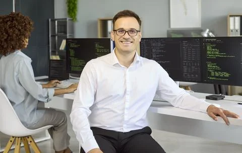 Smiling male programmer in office with code on monitors confident software 스톡 사진