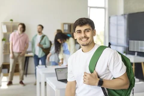 Smiling male student with backpack in classroom peers talking during study Stock Photos