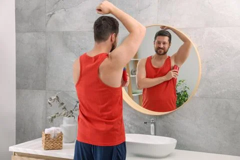 Smiling man applying solid deodorant near mirror at home, back view Stockfoto's