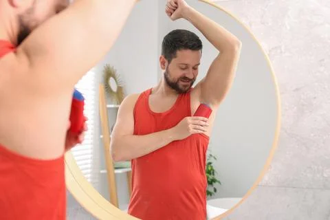 Smiling man applying solid deodorant near mirror at home Stockfoto's