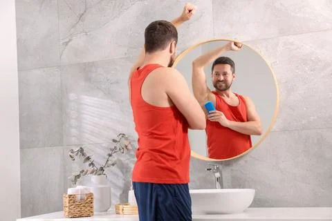 Smiling man applying solid deodorant near mirror at home Stockfoto's