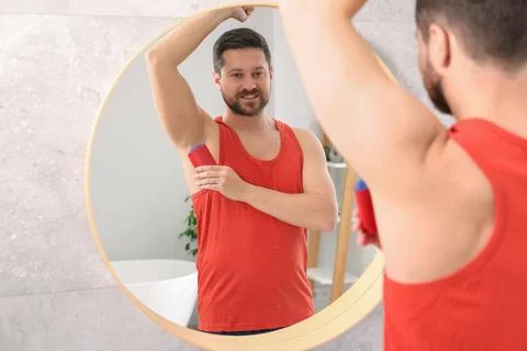 Smiling man applying solid deodorant near mirror at home Stockfoto's