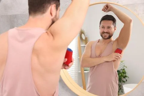 Smiling man applying solid deodorant near mirror at home, back view Stockfoto's