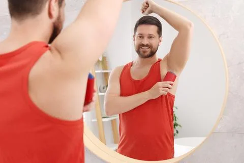 Smiling man applying solid deodorant near mirror at home Stockfoto's
