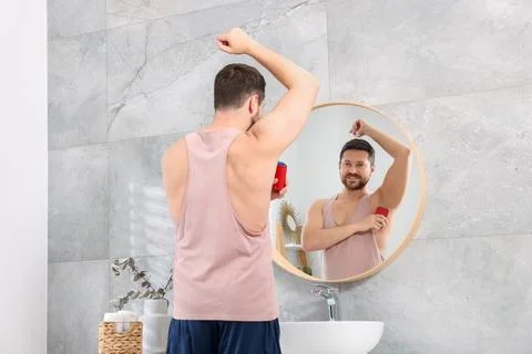 Smiling man applying solid deodorant near mirror at home, back view Stockfoto's