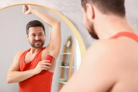 Smiling man applying solid deodorant near mirror at home Stockfoto's