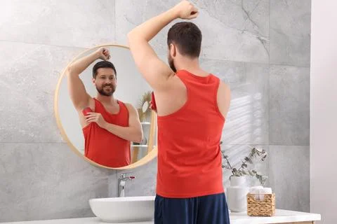 Smiling man applying solid deodorant near mirror at home Stockfoto's