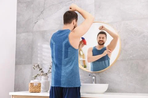 Smiling man applying solid deodorant near mirror at home, back view Stockfoto's