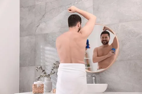 Smiling man applying solid deodorant near mirror in bathroom, back view 스톡 사진