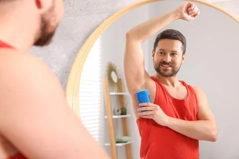 Smiling man applying solid deodorant near mirror at home 스톡 사진
